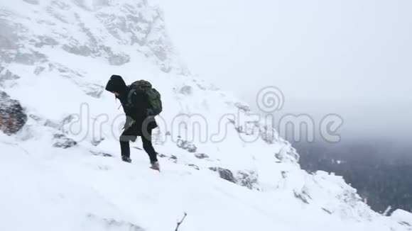 一个年轻人一个游客肩膀上有一个背包上升到一座白雪覆盖的山顶视频的预览图
