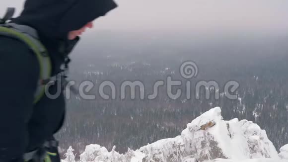 一个背着背包的年轻人爬上了白雪覆盖的山顶视频的预览图