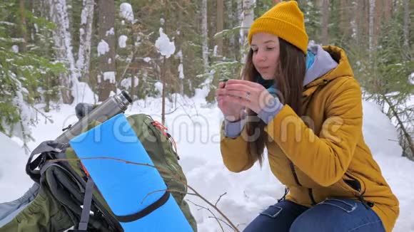 女孩游客在冬天白雪覆盖的森林里喝着热水瓶里的茶视频的预览图