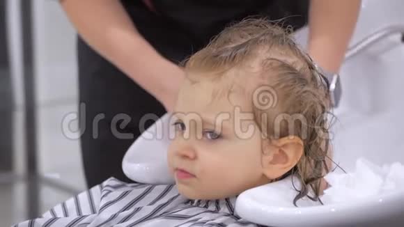 发型师理发师在美容院的椅子上洗一个可爱的小女孩的头美发头部视频的预览图