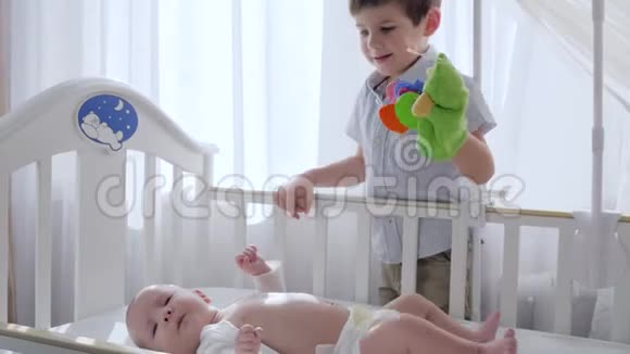 兄弟般的爱抱着玩具的孩子和婴儿一起在小床上玩耍靠近明亮的窗户视频的预览图