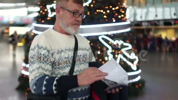 一个留着灰胡子的人正在等待他的航班在圣诞节和新年期间到达国际机场视频的预览图