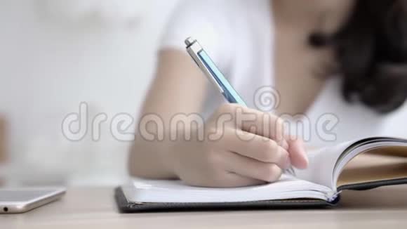 坐在客厅里学习的亚洲女人的特写手在家里桌上写笔记本和日记视频的预览图