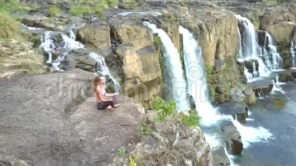 少女坐在瀑布旁陡峭的悬崖上摆着莲花视频的预览图
