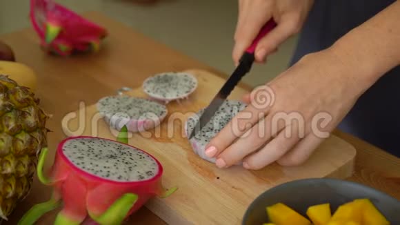 慢镜头一位年轻女子将火龙果切成方块许多热带水果摆在桌上视频的预览图