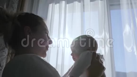 母子关系幸福的妈妈把宝宝举在窗外的房间里视频的预览图