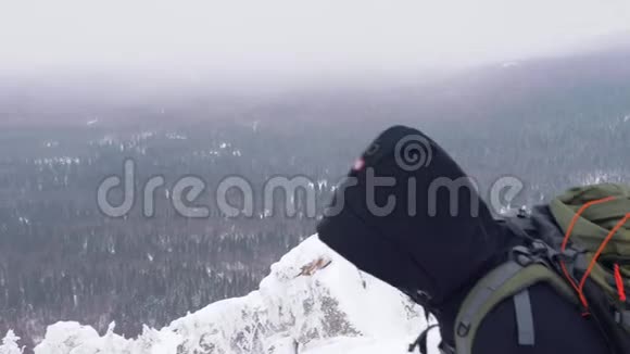 一个背着背包的年轻人爬上了白雪覆盖的山顶视频的预览图