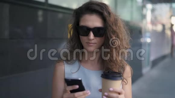 迷人的年轻女孩在夏天的街道上发短信喝咖啡视频的预览图