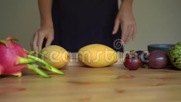 慢镜头拍摄一位年轻女子剥芒果和许多热带水果放在桌子上视频的预览图