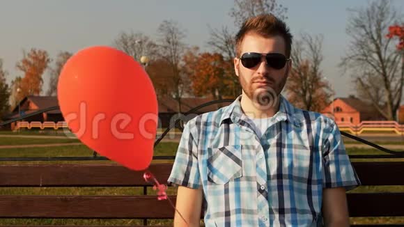 一个满脸胡须的人手里拿着一个红色气球坐在长凳上视频的预览图
