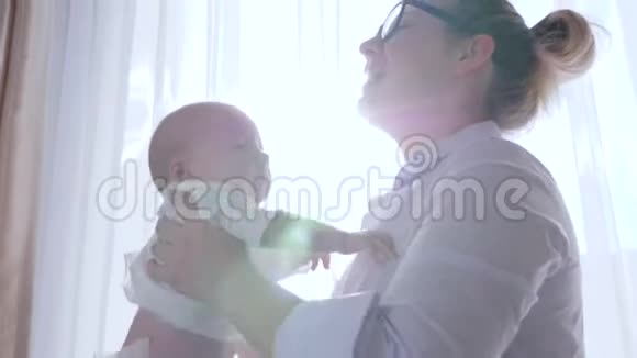 父母的爱年轻的妈妈在家靠窗的阳光下把孩子抱起来视频的预览图
