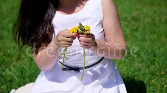 夏天近在眼前一位身穿白色礼服的黑发女子坐在绿色的草坪上草地上编织着一个黄色的蒲公英花圈视频的预览图