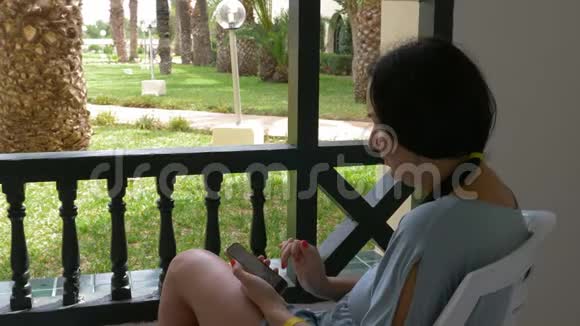 成年女性使用智能手机夏天休息在室外阳台现代女性看手机旅游博客视频的预览图