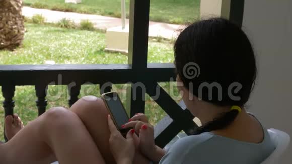 使用手机在室外阳台的社交网络中聊天的Brunette妇女视频的预览图