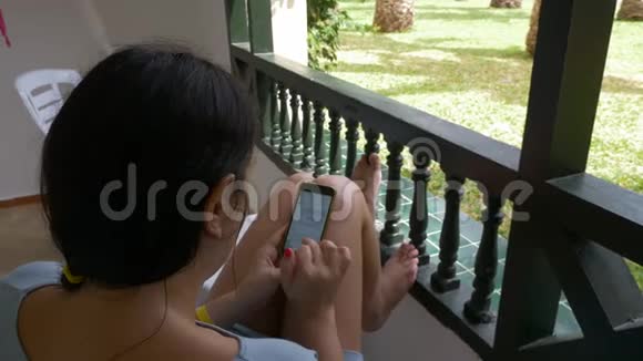 年轻女子坐在室外阳台上使用手机女人在电话里发短信肩景高角度视频的预览图