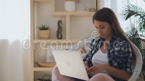 年轻的美国女人在笔记本电脑上打字坐在公寓里社交媒体上交流视频的预览图