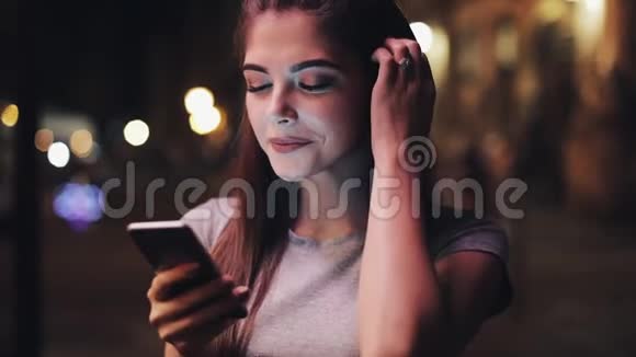 漂亮的年轻女人用智能手机看着相机她站在夜城的街道上视频的预览图