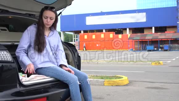 坐在汽车后备箱里吃饭的年轻女子视频的预览图