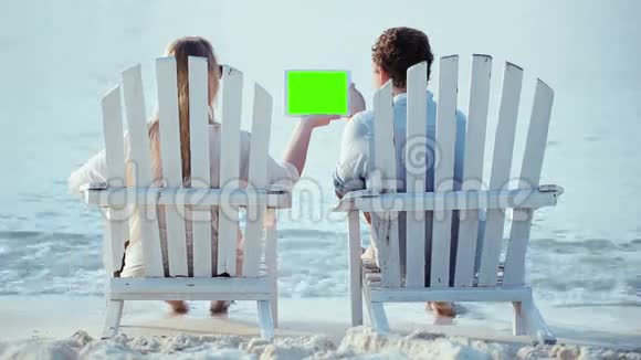 女人和男人坐在沙滩上看着视频的预览图