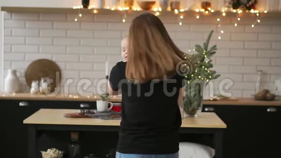 妈妈抱着宝宝孩子微笑着看着心爱的妈妈圣诞节时一起站在白色的厨房里视频的预览图