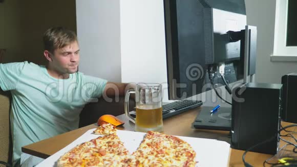 一个满足的人坐在家里的沙发上喝啤酒吃披萨用电脑上网看着一个视频的预览图