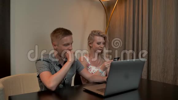 男人和女人坐在沙发上用笔记本电脑上的信用卡在线购物视频的预览图