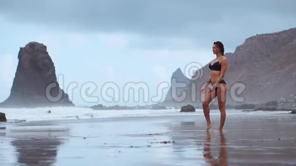 一位美丽的女子在海滩上用黑色的火山沙做体操练习健康的身体视频的预览图