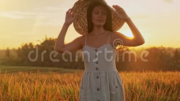 特写一位戴着长发戴着帽子在麦田里散步的幸福微笑的女人的画像视频的预览图
