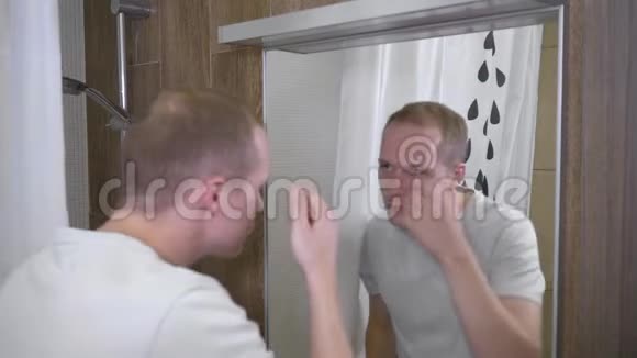 一个年轻英俊的男人那个人在镜子里看到他额头上的痤疮男人用遮瑕膏覆盖痤疮4k慢动作视频的预览图