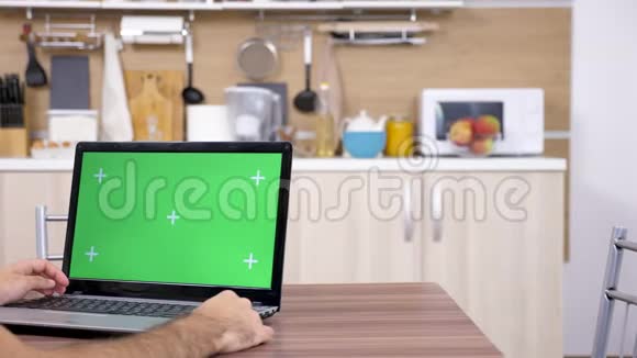 厨房里的男人看着手提电脑用绿色屏幕模拟视频的预览图