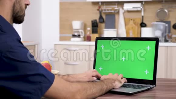 厨房里的男人用绿色屏幕在笔记本电脑键盘上打字视频的预览图