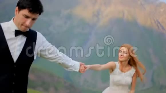 可爱的新婚夫妇在美丽的群山背景下漫步在草地上视频的预览图