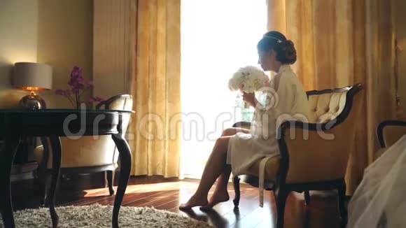 年轻的新娘坐在一家豪华酒店的窗边手里拿着一束鲜花视频的预览图