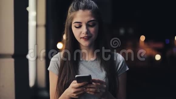 迷人的年轻女子拨通一个电话号码在夜城街道上的智能手机上交谈美丽美丽视频的预览图