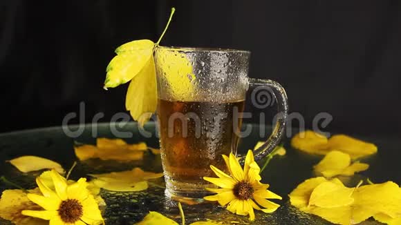 在秋天的景色中一个透明的玻璃杯在热茶的雨中湿漉漉的黄色的落叶黄色的花朵视频的预览图