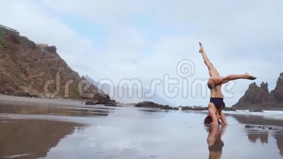 美丽的女人在沙滩上与黑沙表演体操练习健康的生活方式和视频的预览图