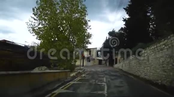 从一辆移动的汽车在一条狭窄的街道上看在一个阴天的雨后有房子路灯和路标塞浦路斯视频的预览图