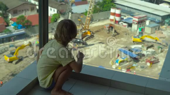 一个小男孩坐在有玻璃墙的阳台上看着一栋多层建筑的建造视频的预览图