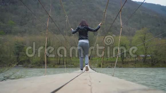 少女旅人渡江上悬桥木渡河渡女子徒步旅行者视频的预览图