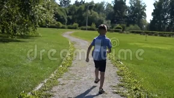 这个男孩在阳光明媚的天气里沿着公园的草地跑步心情很好慢动作视频的预览图