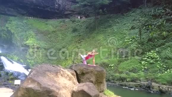 女孩在绿色的山坡上高高的岩石上摆瑜伽姿势视频的预览图