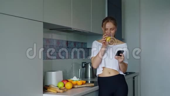 美丽的女孩喝着新鲜的橙汁从玻璃女人用智能手机视频的预览图