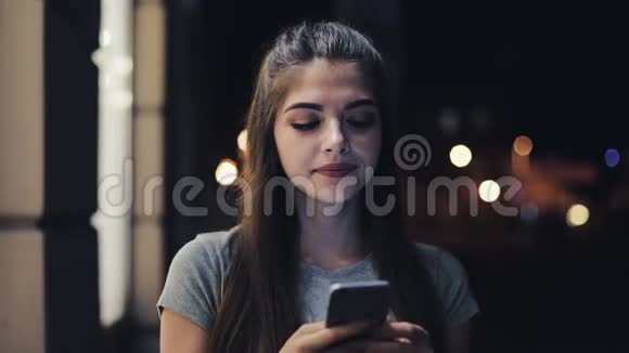 迷人的年轻女性使用智能手机行走在夜城的街道上对这条信息做出了愉快的反应现代视频的预览图