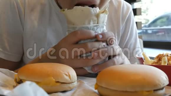 青少年在快餐店里吃一个大鸡卷桌子上有大的芝士汉堡和薯条视频的预览图