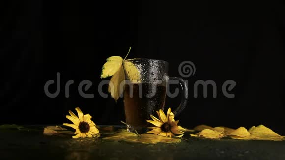 一个透明的玻璃杯是湿的在热茶的雨中在秋天的风景中黄色的落叶黄色的花视频的预览图