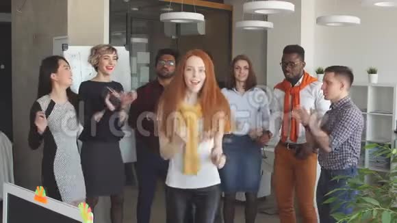 红发女孩经理穿着时尚的服装正在娱乐他的同事在工作中跳舞视频的预览图