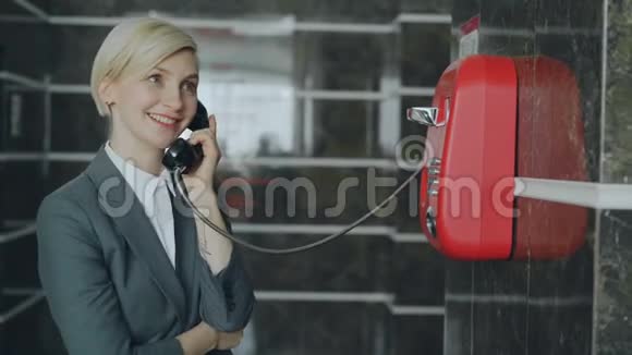 在酒店大堂的接待处一位开朗的女商人与带有线红电话的工作人员交谈商务旅行和视频的预览图