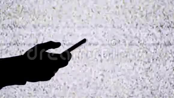 一只手拿着智能手机在电视屏幕背景上的剪影带有白色的静态噪音视频的预览图