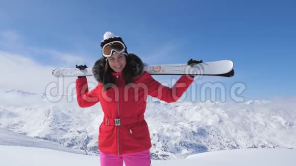 微笑的漂亮女人滑雪站在山坡上肩膀上举着滑雪板视频的预览图