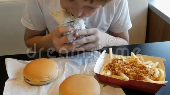 青少年在快餐店里吃一个大鸡卷桌子上有大的芝士汉堡和薯条视频的预览图